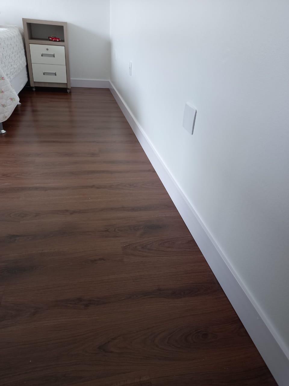 Piso laminado escuro com rodapé branco em quarto